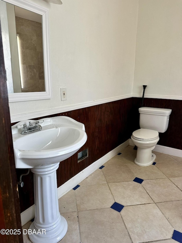 bathroom with tile patterned floors, toilet, and wood walls