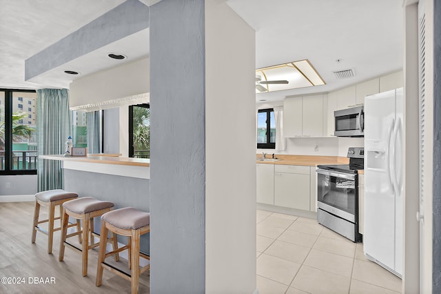 kitchen with stainless steel appliances, sink, a kitchen breakfast bar, butcher block countertops, and white cabinetry