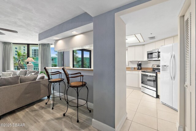 kitchen with stainless steel appliances, white cabinets, open floor plan, baseboards, and a ceiling fan
