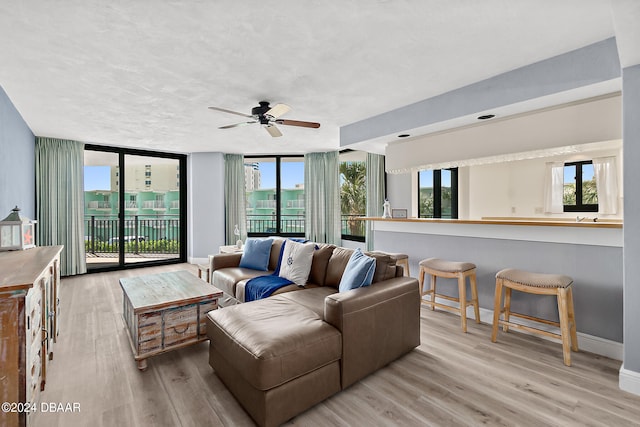 living room featuring ceiling fan, light hardwood / wood-style flooring, and a wall of windows