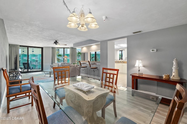 dining room featuring light wood-type flooring, a chandelier, ceiling fan, baseboards, and a textured ceiling