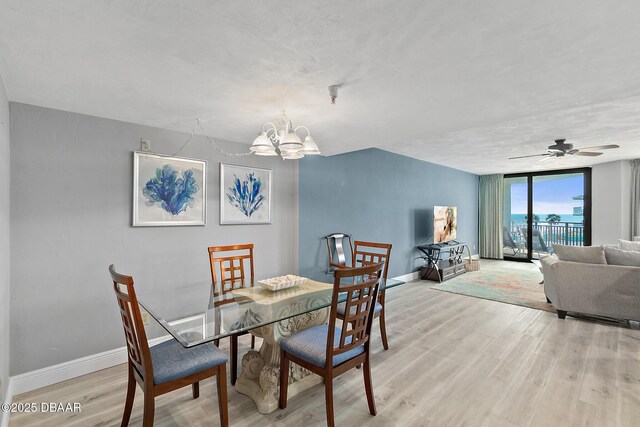dining space featuring light wood-style floors, baseboards, a chandelier, ceiling fan, and expansive windows