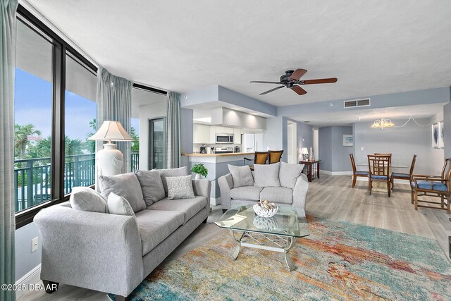 living area with baseboards, light wood-style flooring, and a ceiling fan