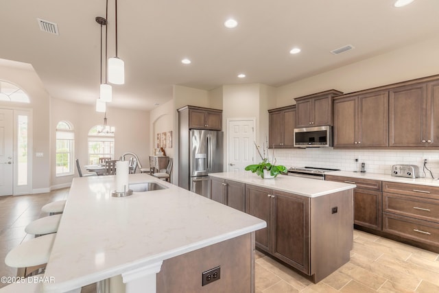 kitchen with appliances with stainless steel finishes, a kitchen breakfast bar, backsplash, hanging light fixtures, and a kitchen island with sink