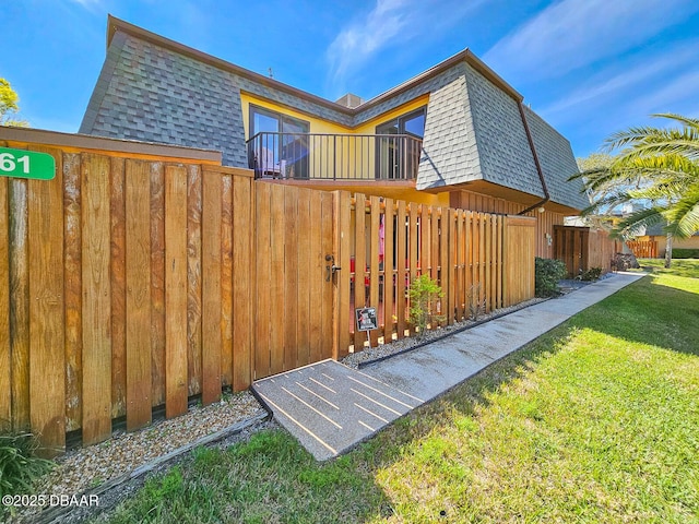 view of side of property with roof with shingles, mansard roof, a lawn, fence, and a balcony