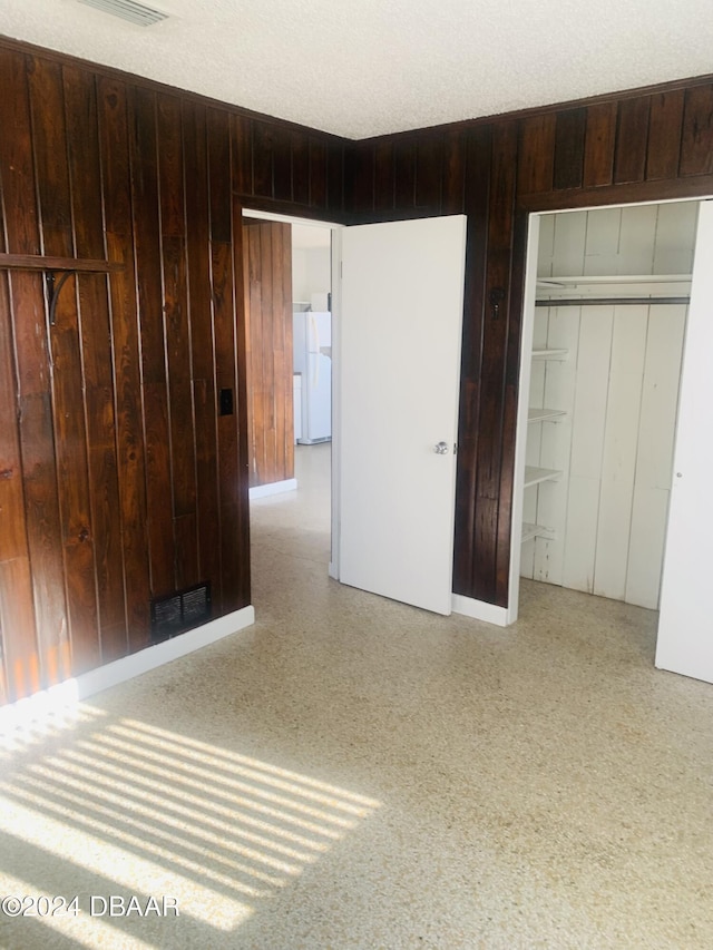 interior space with visible vents, wood walls, freestanding refrigerator, a closet, and a textured ceiling