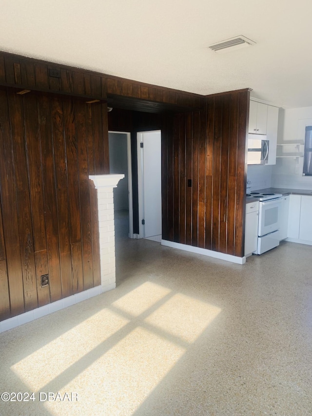 spare room featuring wooden walls, light speckled floor, and visible vents