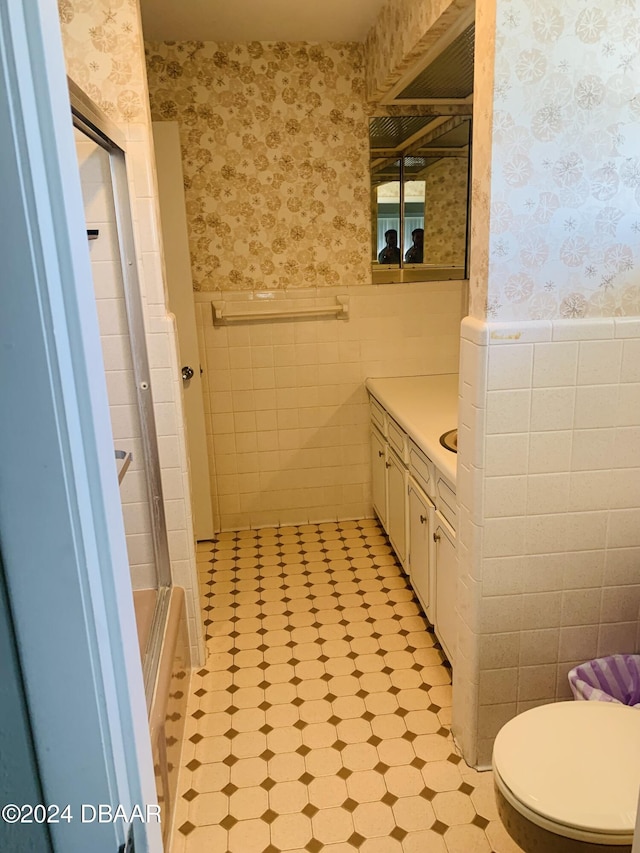 full bathroom featuring wallpapered walls, tile walls, an enclosed shower, and a wainscoted wall
