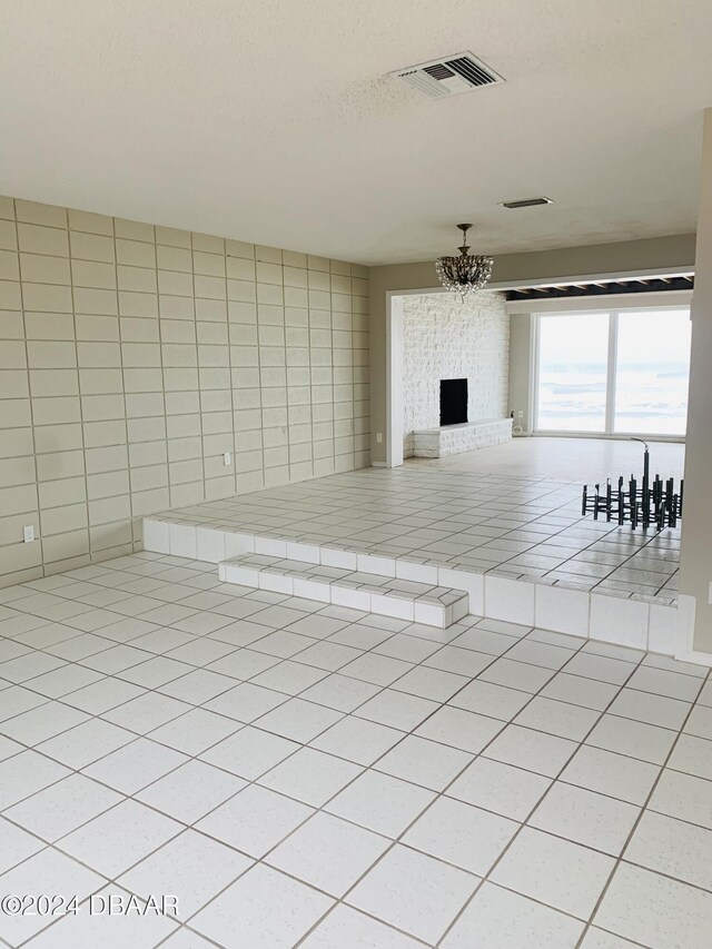 unfurnished living room featuring visible vents, an inviting chandelier, light tile patterned flooring, and a fireplace
