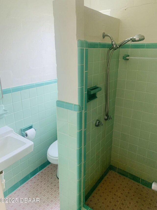 full bathroom with tiled shower, toilet, tile walls, and wainscoting