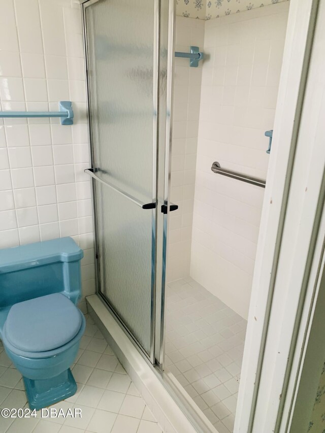 bathroom featuring tile patterned flooring, tile walls, toilet, and a stall shower