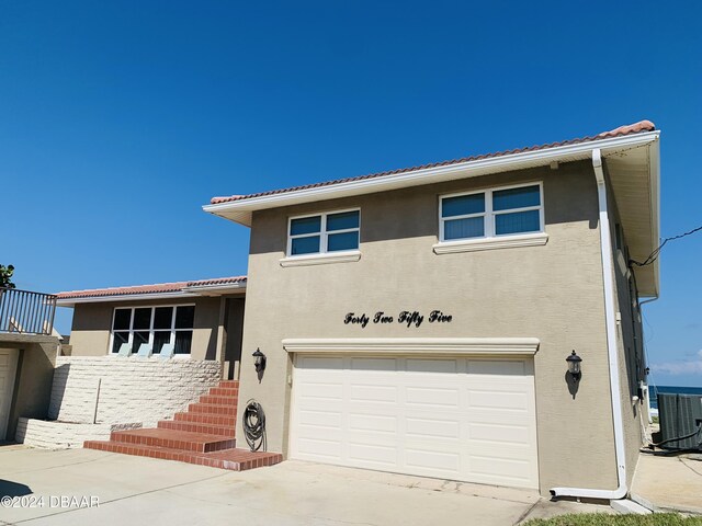 view of front facade featuring concrete driveway, central air condition unit, a garage, and stucco siding