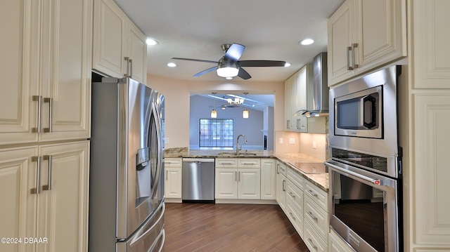 kitchen featuring light stone counters, dark wood-style flooring, stainless steel appliances, a sink, and wall chimney exhaust hood