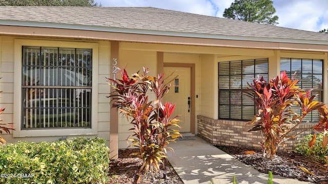 property entrance featuring roof with shingles and brick siding