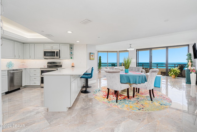 kitchen featuring a raised ceiling, a breakfast bar area, backsplash, kitchen peninsula, and stainless steel appliances