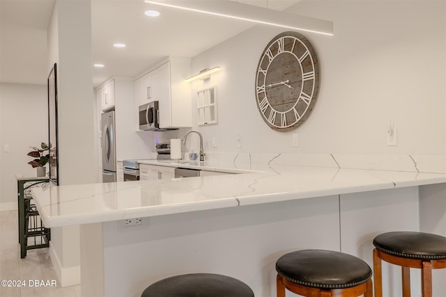 kitchen with a kitchen breakfast bar, kitchen peninsula, white cabinetry, and appliances with stainless steel finishes