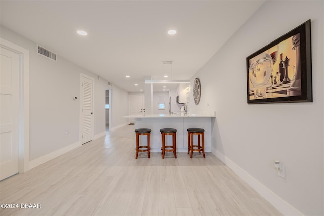 kitchen with a breakfast bar, kitchen peninsula, light wood-type flooring, decorative light fixtures, and white cabinetry