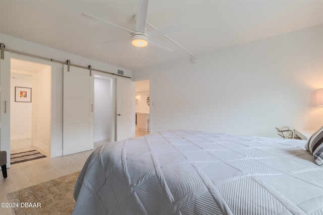 bedroom featuring ensuite bathroom, a barn door, light hardwood / wood-style floors, and ceiling fan