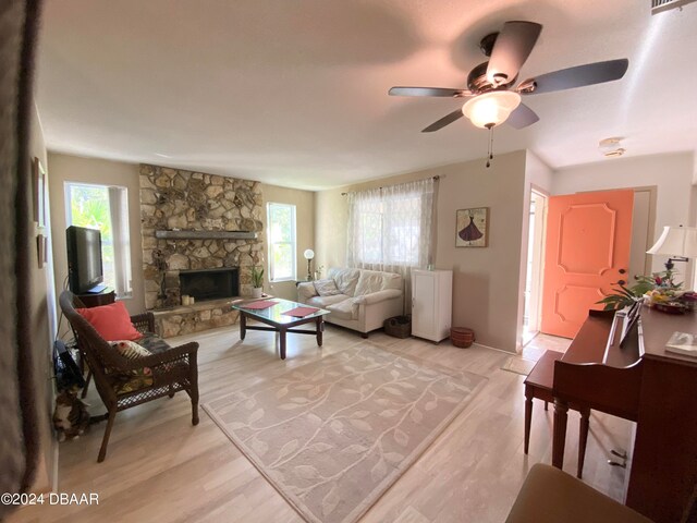 living room with a stone fireplace, light hardwood / wood-style flooring, and ceiling fan