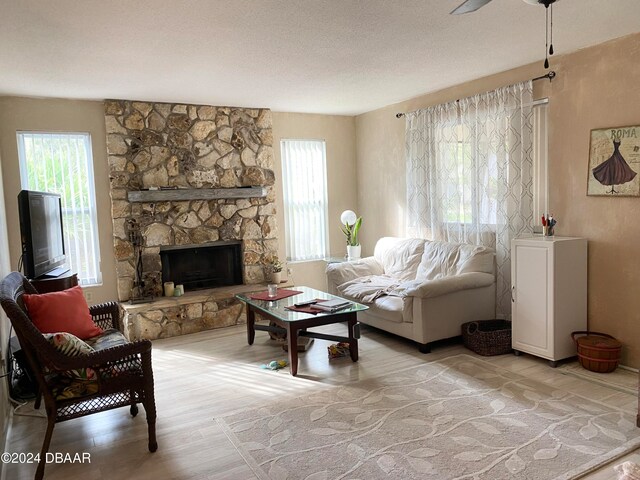 living room featuring a stone fireplace, light hardwood / wood-style floors, a textured ceiling, and a healthy amount of sunlight