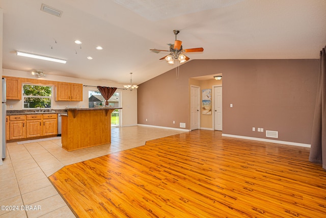 kitchen featuring ceiling fan with notable chandelier, light hardwood / wood-style floors, vaulted ceiling, stainless steel dishwasher, and decorative light fixtures