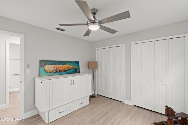 bedroom featuring light hardwood / wood-style flooring, ceiling fan, and multiple closets