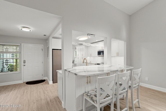 kitchen featuring a breakfast bar, kitchen peninsula, light wood-type flooring, light stone counters, and white cabinetry