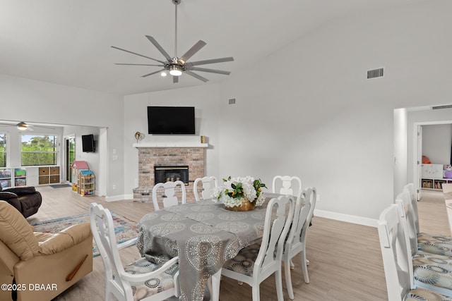 dining room with a fireplace, high vaulted ceiling, and light hardwood / wood-style flooring