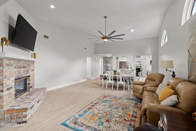 living room with a fireplace, ceiling fan, light hardwood / wood-style flooring, and a towering ceiling