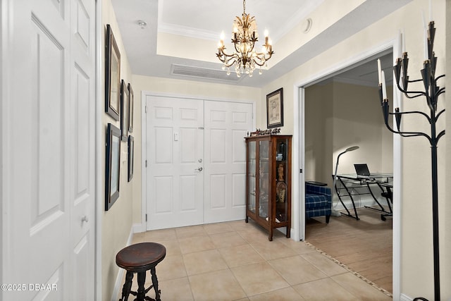 tiled foyer featuring a chandelier, ornamental molding, and a raised ceiling