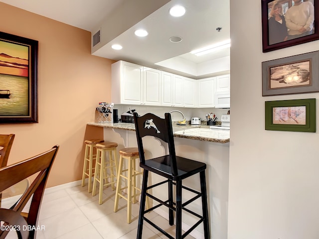 kitchen featuring white cabinetry, white appliances, light stone countertops, and a kitchen breakfast bar