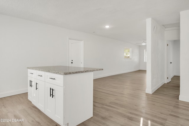 kitchen with a center island, light stone countertops, light hardwood / wood-style floors, and white cabinets