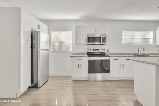 kitchen with stainless steel appliances, light hardwood / wood-style floors, white cabinets, and a textured ceiling