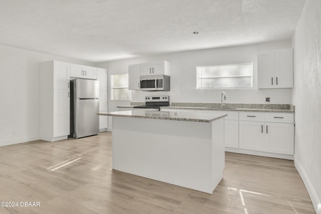 kitchen featuring white cabinetry, appliances with stainless steel finishes, a textured ceiling, light hardwood / wood-style flooring, and a center island