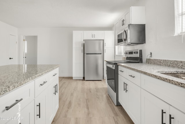 kitchen with light hardwood / wood-style flooring, appliances with stainless steel finishes, light stone counters, and white cabinets