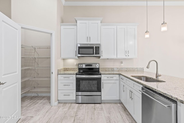 3402 Torre Blvd, New Smyrna Beach, FL 32168 - kitchen featuring appliances with stainless steel finishes, a sink, ornamental molding, white cabinets, and light wood-style flooring