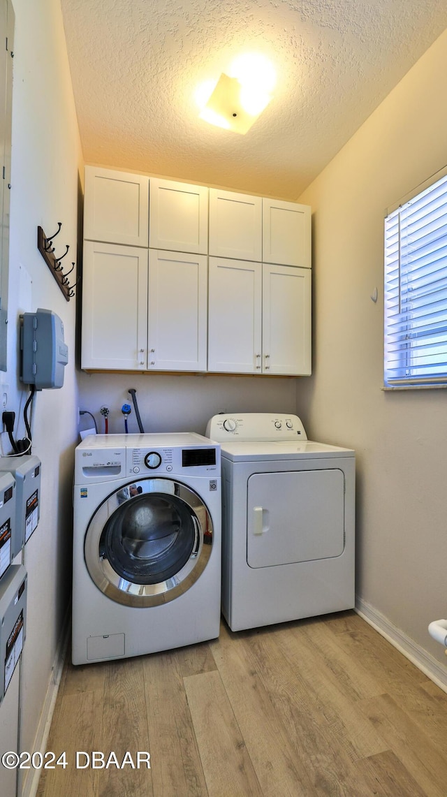 laundry room with independent washer and dryer, cabinets, a textured ceiling, and light wood-type flooring