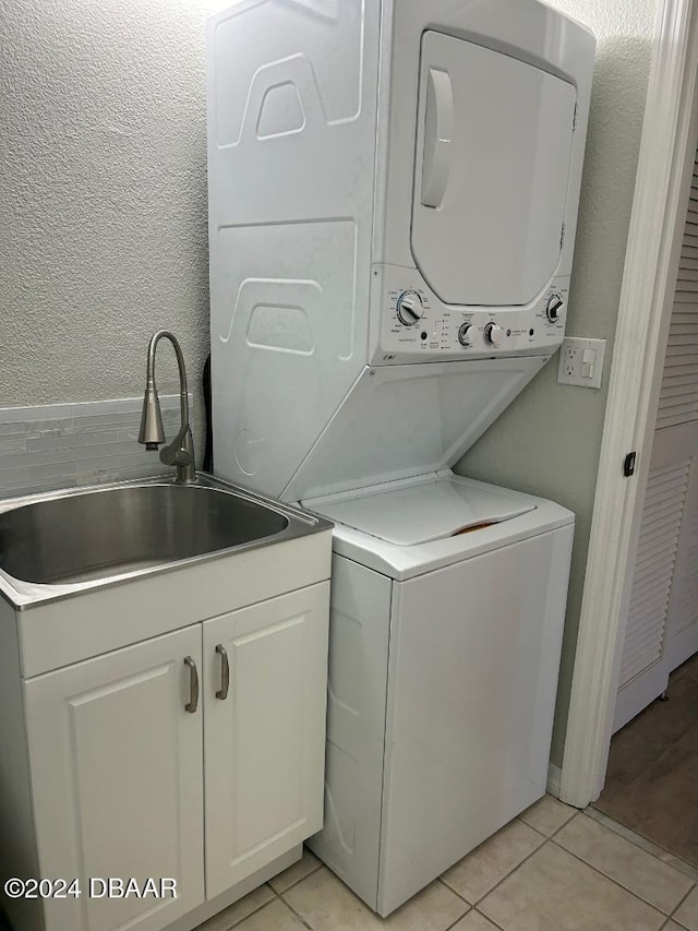 washroom featuring cabinets, light tile patterned floors, stacked washer and dryer, and sink