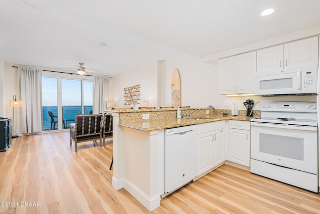 kitchen featuring light stone countertops, light hardwood / wood-style flooring, kitchen peninsula, white appliances, and a water view