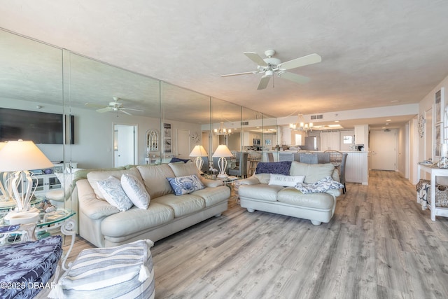 living room featuring ceiling fan with notable chandelier and light wood-type flooring