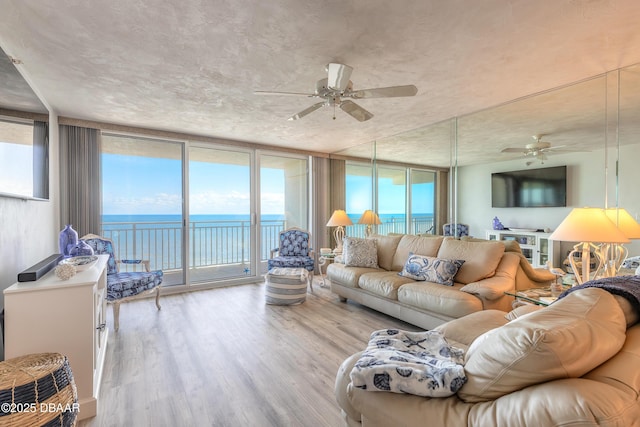 living room with floor to ceiling windows, a water view, ceiling fan, and light wood-type flooring