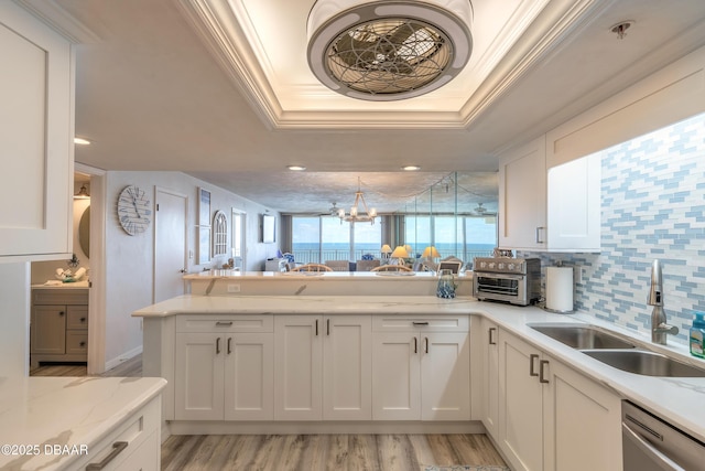 kitchen with sink, crown molding, white cabinets, stainless steel dishwasher, and a raised ceiling