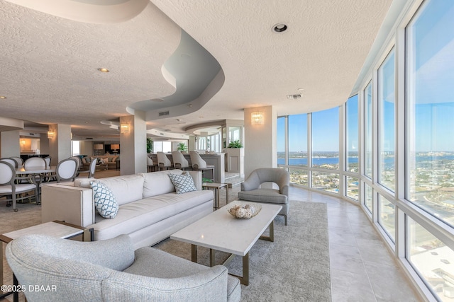 tiled living room featuring expansive windows, a water view, and a textured ceiling