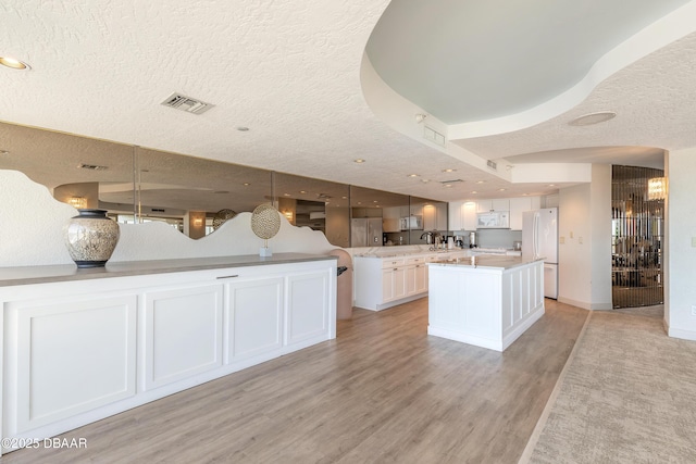 kitchen with a kitchen island with sink, pendant lighting, white appliances, light hardwood / wood-style floors, and white cabinets