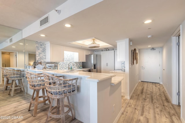 kitchen featuring stainless steel fridge, a breakfast bar, white cabinetry, tasteful backsplash, and kitchen peninsula