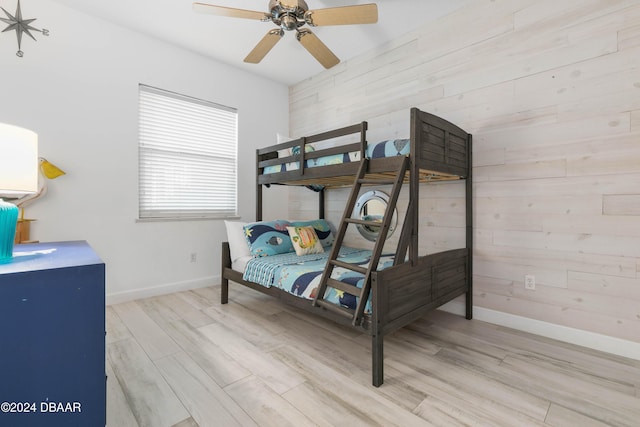 bedroom with wood walls, ceiling fan, and light wood-type flooring