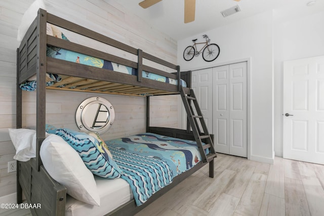 bedroom featuring ceiling fan, light wood-type flooring, a closet, and wood walls