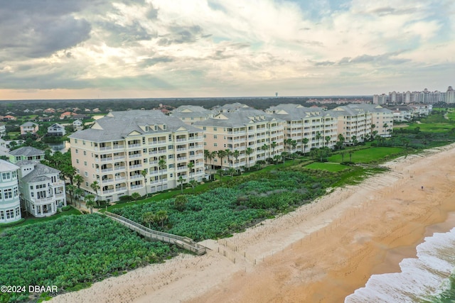 aerial view at dusk featuring a water view and a beach view