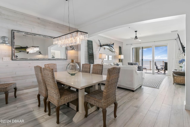 dining area with light wood-type flooring, ceiling fan, crown molding, and wood walls