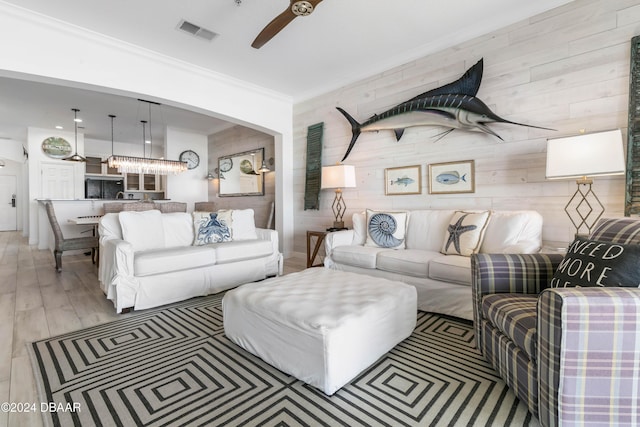 living room featuring ceiling fan, crown molding, wood walls, and light wood-type flooring